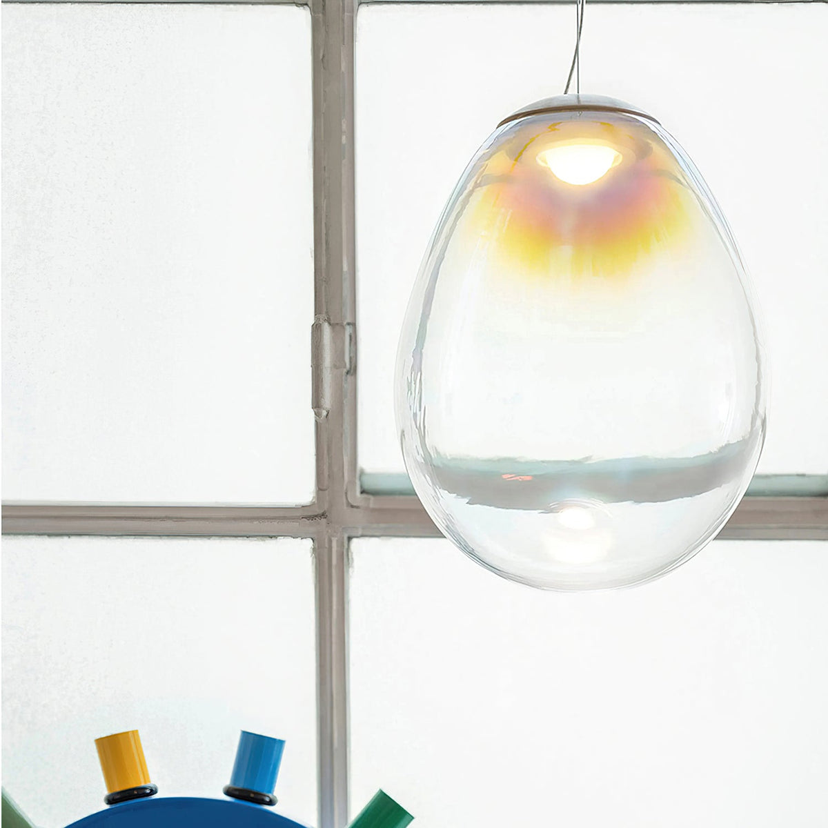 Close view of a Clérachic clear glass pendant in front of a grid window, with a gold and pink gradient near the top of the shade.