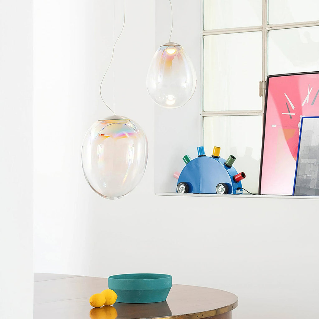 Two of these Clérachic glass pendants hang by a window with a pink poster, above a table with a teal bowl and two lemons.