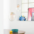 Two of these Clérachic glass pendants hang by a window with a pink poster, above a table with a teal bowl and two lemons.