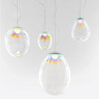 Four Clérachic glass teardrop pendants of different sizes hang at staggered heights against a pale grey wall, each with a coloured top.