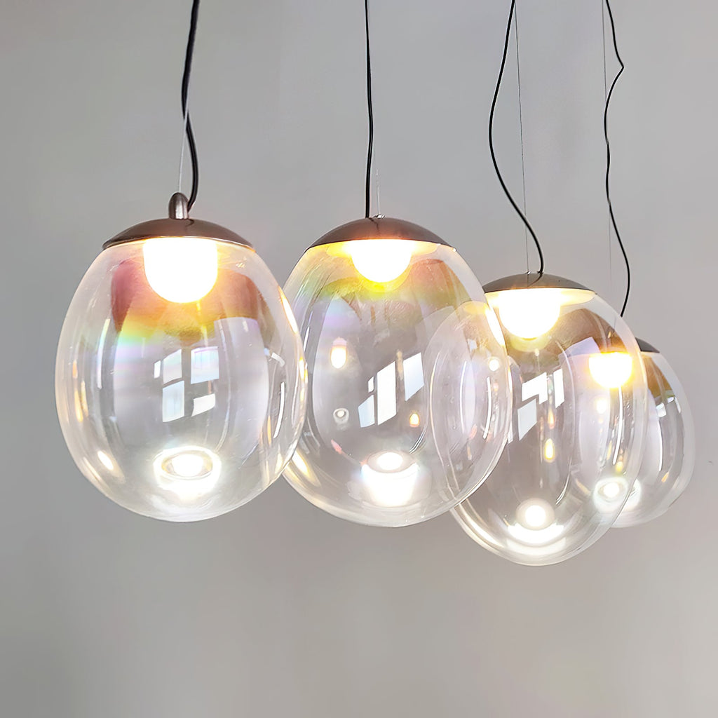 A lit cluster of Clérachic clear glass pendants hangs from dark cords, with reflections of a window on the glass and a warm bulb in each.
