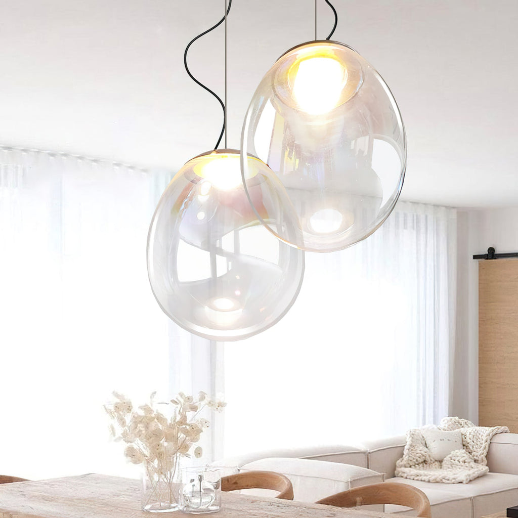 These Clérachic glass pendants hang over a pale wooden table, with dried flowers in a glass vase and a cream sofa behind.
