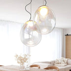 These Clérachic glass pendants hang over a pale wooden table, with dried flowers in a glass vase and a cream sofa behind.