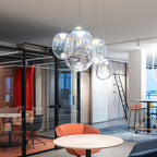 A tight group of Clérachic clear glass pendants hangs in a bright open office with glass partitions, a red curtain and a round white table.
