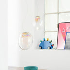Two Clérachic glass teardrop pendants hang beside a grid window, above a table with a teal bowl and a blue shelf ornament.