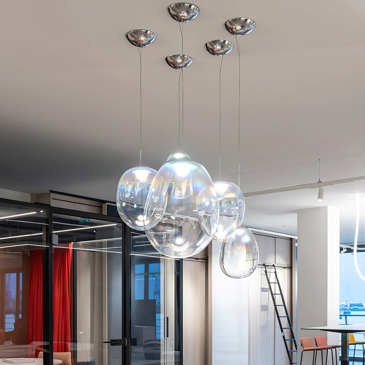Five Clérachic glass pendants hang from small chrome ceiling canopies in a glass-walled office with a ladder and tall tables behind.
