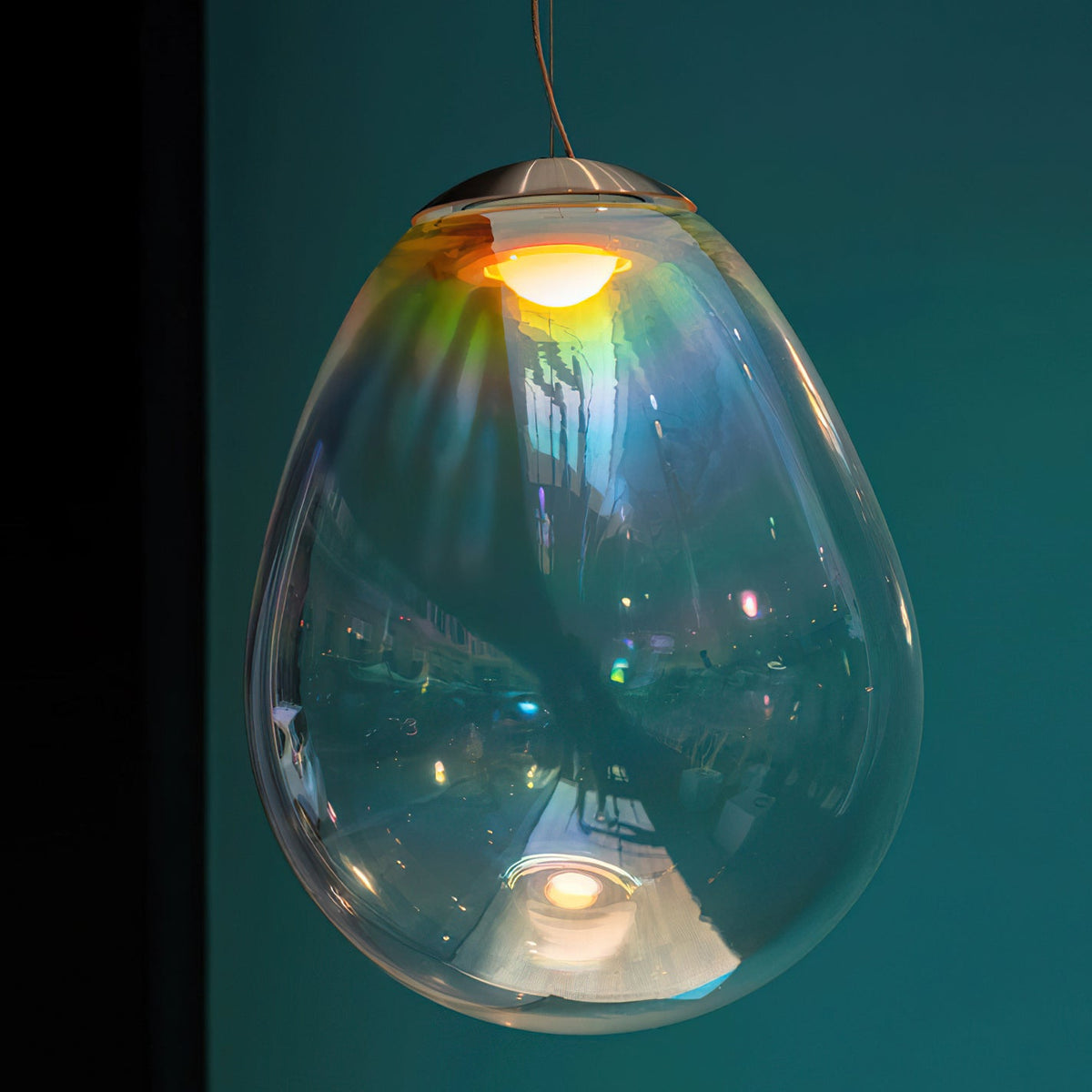 Close view of a Clérachic glass pendant against a deep teal wall, its clear shade reflecting a room and a gold glow from the bulb.