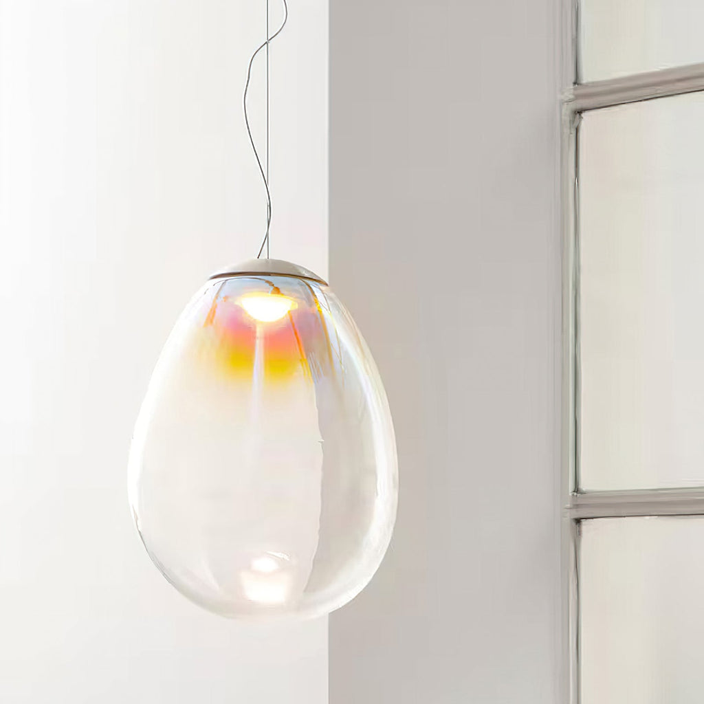 This Clérachic glass pendant hangs on a thin cord near a window, its clear egg-shaped shade tinted gold and pink at the top.