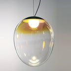 Close view of the lit bulb inside a Clérachic clear glass pendant, with an amber to clear gradient and a dark cap above.