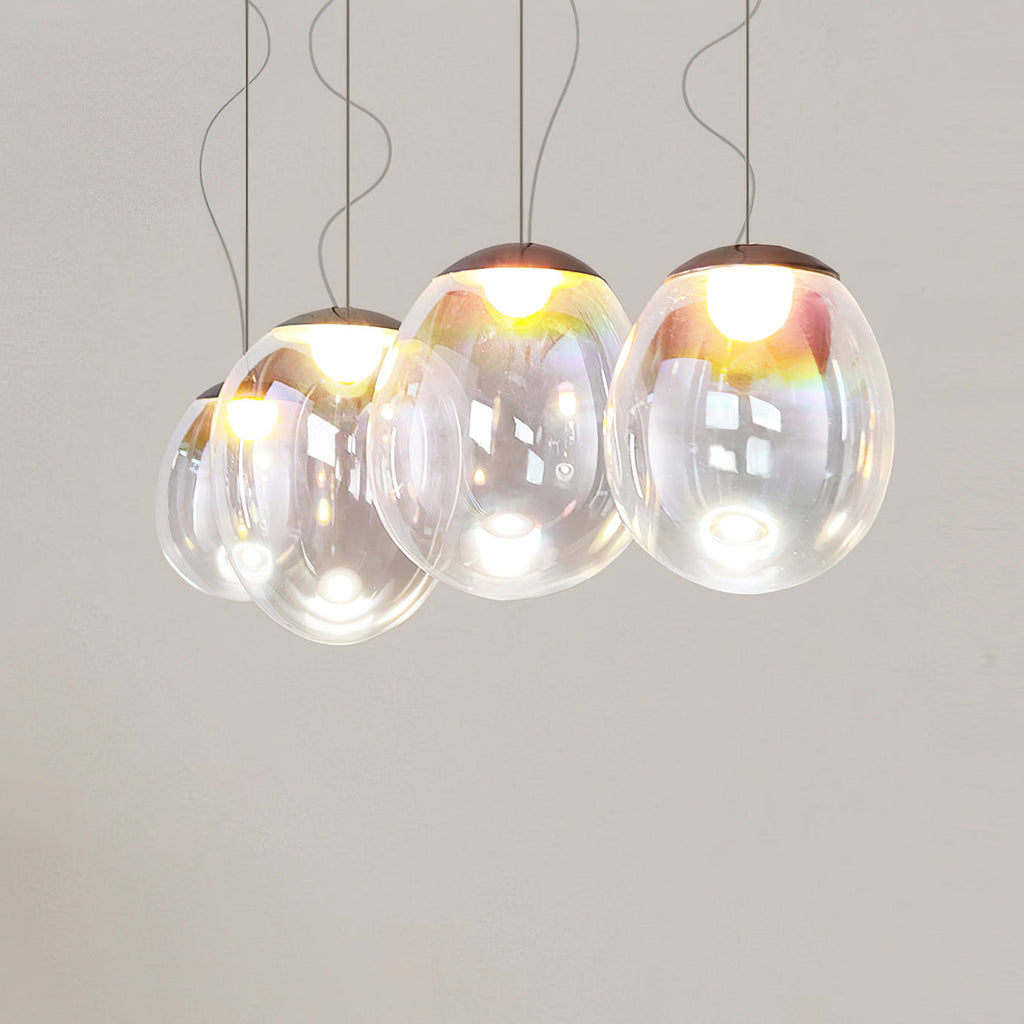 A lit group of Clérachic clear glass pendants hangs close together on thin cords against a warm grey wall.