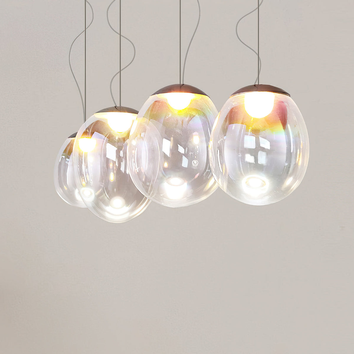 A lit group of Clérachic clear glass pendants hangs close together on thin cords against a warm grey wall.