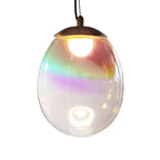 Close view of a lit Clérachic glass pendant, with green, purple and gold colour bands across the clear shade below a dark cap.