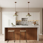 Two green Clérachic pendants with walnut caps hang above a kitchen island with a walnut-panelled front and slim stools.