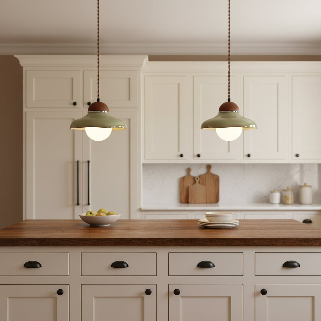 Close shot of two Clérachic green ceramic pendants lit above cream cabinets and a walnut counter with a fruit bowl.