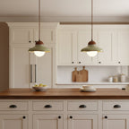Close shot of two Clérachic green ceramic pendants lit above cream cabinets and a walnut counter with a fruit bowl.