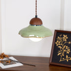 Clérachic green pendant with a wavy ceramic rim, above a walnut sideboard with a framed gold botanical print.