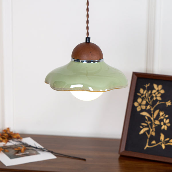 Clérachic green pendant with a wavy ceramic rim, above a walnut sideboard with a framed gold botanical print.