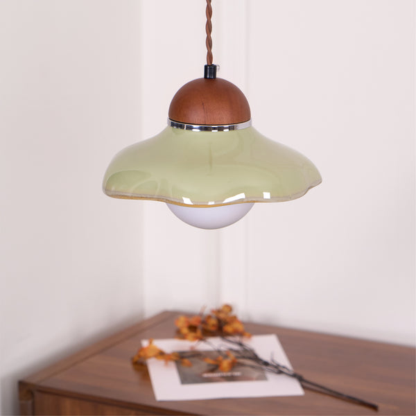 Wavy-edged green ceramic Clérachic pendant with a walnut cap, hanging in a corner above a wooden sideboard.