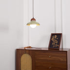 Distant view of this Clérachic green pendant above a walnut sideboard with a rattan door panel and a framed print.