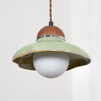 Close view of the green ceramic shade, walnut cap and frosted white globe of this Clérachic pendant on a light wall.