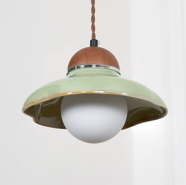 Close view of the green ceramic shade, walnut cap and frosted white globe of this Clérachic pendant on a light wall.
