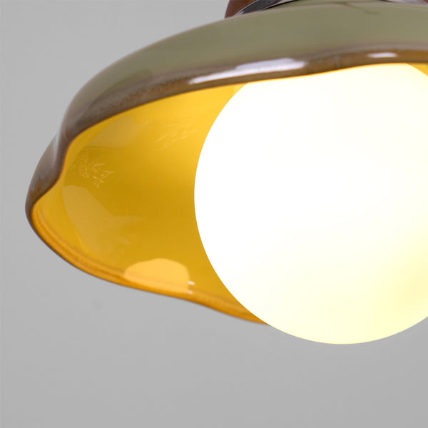 Close view under the wavy rim of this Clérachic pendant, with its yellow glazed interior and a glowing frosted globe.
