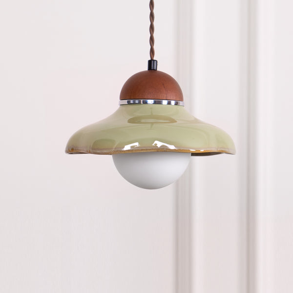 Clérachic green ceramic pendant with a walnut-coloured cap and a white globe, centred against a pale wall.