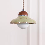 Clérachic green ceramic pendant with a walnut-coloured cap and a white globe, centred against a pale wall.