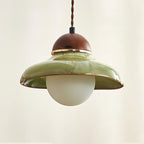 Clérachic pendant with a wavy green ceramic shade, a walnut cap and a gold rim, against a warm cream wall.