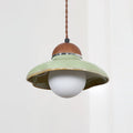 Clérachic green ceramic pendant with an unlit white globe, seen against a pale curtain.