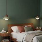 Two Clérachic green pendants light a bedroom with a deep green wall, a wooden bed and terracotta cushions.