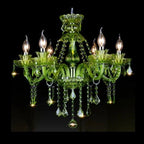 Clérachic six-arm green glass chandelier with candle bulbs and faceted crystal drops, lit against a black backdrop.