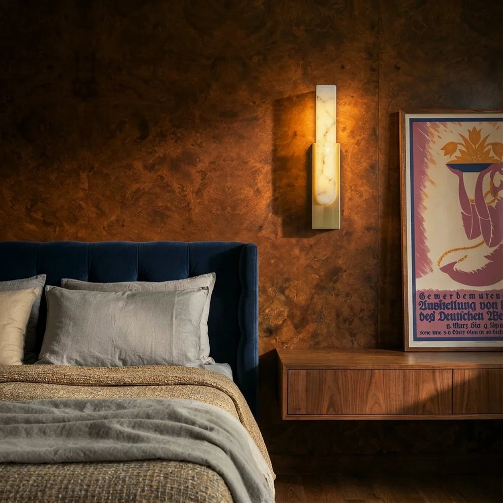 Clérachic gold-framed alabaster sconce lit beside a bed, its warm glow set against a burl wood headboard wall.