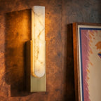 Close view of the Clérachic gold-framed alabaster sconce mounted on richly grained burl wood paneling.