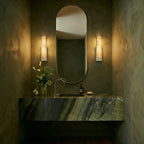 Pair of Clérachic white-framed alabaster sconces flanking an oval mirror above a green marble bathroom vanity.
