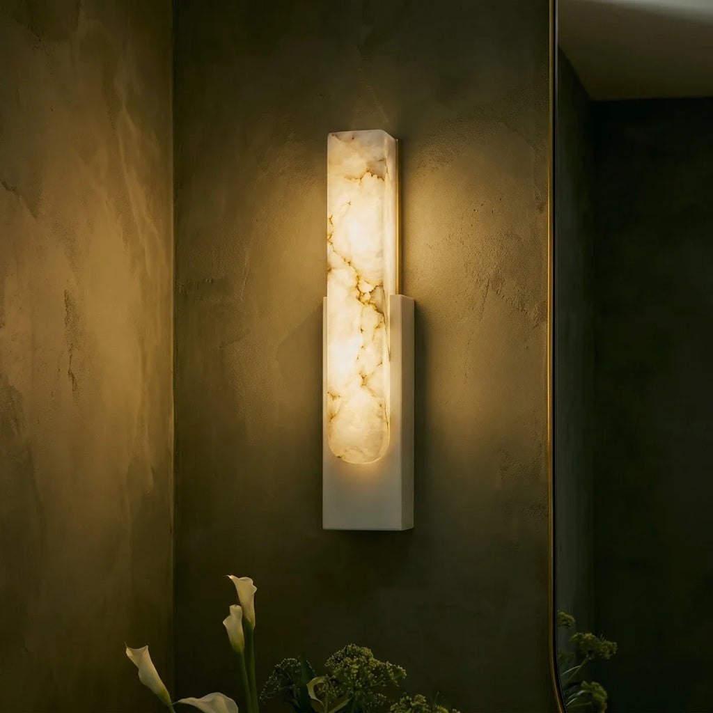 Close view of a Clérachic white-framed alabaster sconce glowing against a dark green plaster wall with calla lilies.