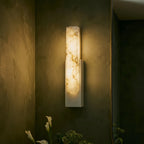 Close view of a Clérachic white-framed alabaster sconce glowing against a dark green plaster wall with calla lilies.