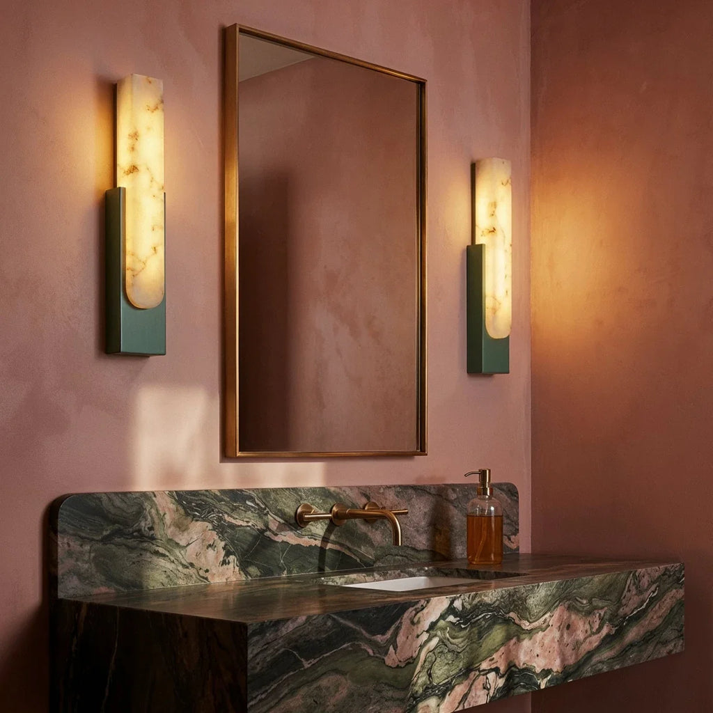 Pair of Clérachic green-framed alabaster sconces flanking a mirror above a green marble vanity on a blush wall.