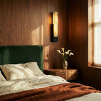 Clérachic black-framed alabaster sconce glowing beside a bed with a green velvet headboard in a walnut bedroom.