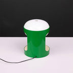 Clérachic table lamp in a brighter, glossier green on a white surface against a black backdrop, with a dark cord running to the front.