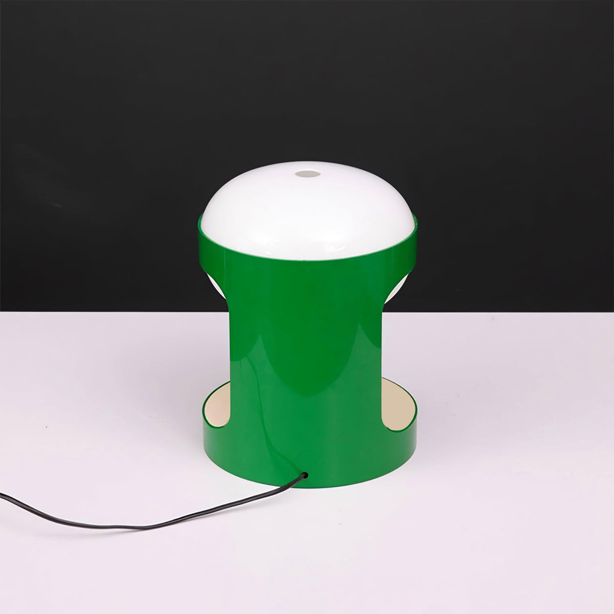 Clérachic table lamp in a brighter, glossier green on a white surface against a black backdrop, with a dark cord running to the front.