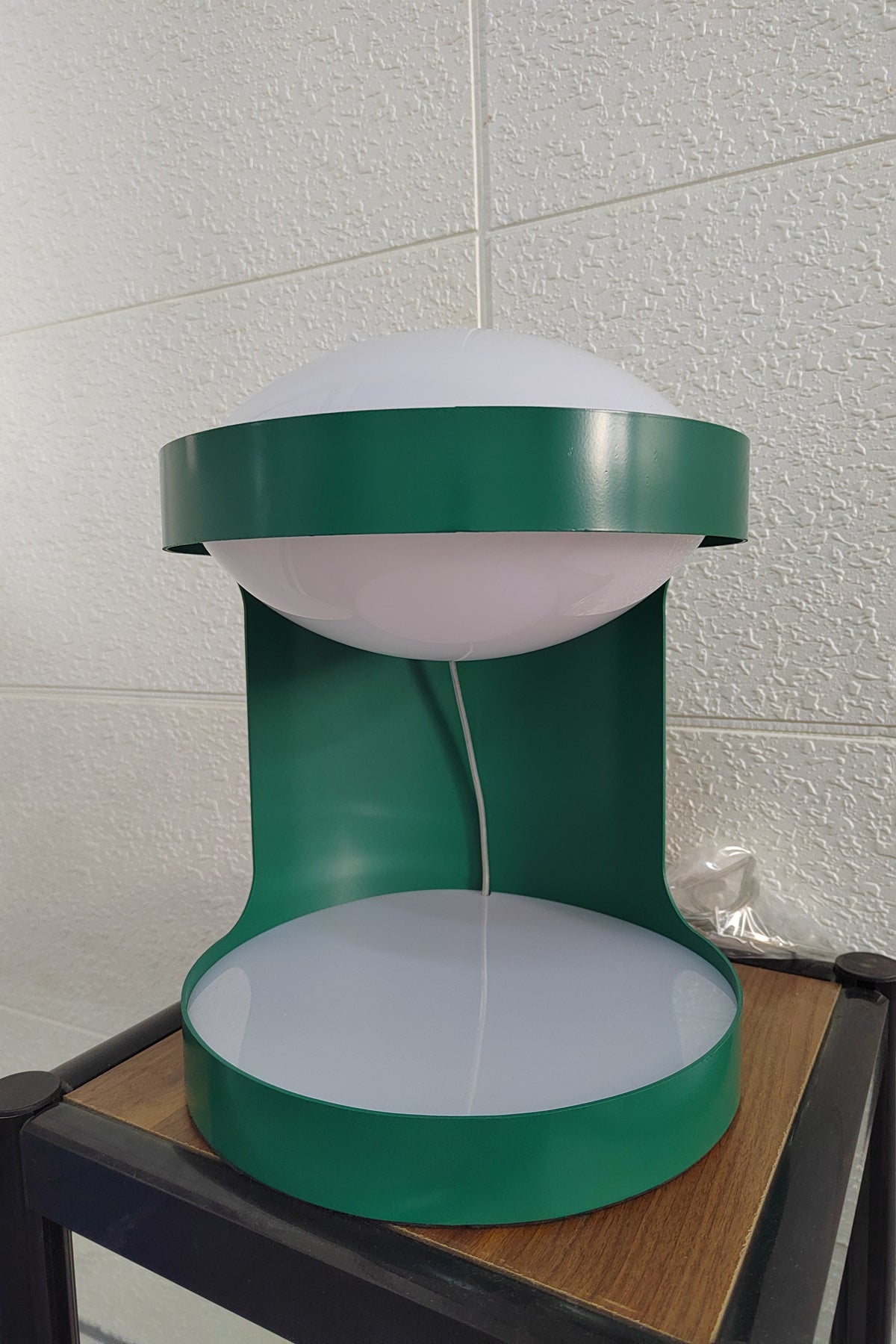 Front view of this Clérachic table lamp on a dark wood-top stand in front of a white brick-pattern wall, its dome unlit.