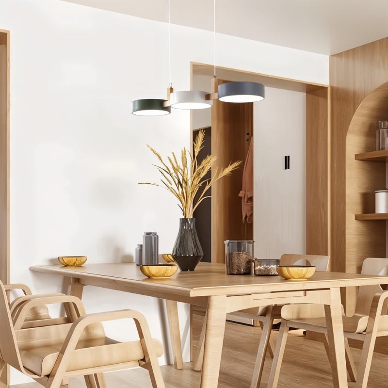 Clérachic's three-drum pendant hangs above a light oak dining table set with woven place mats and dried grasses.