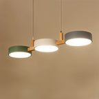 Clérachic's three-drum pendant in green, white and grey shades hangs from a slim wood crossbar on a tan backdrop.