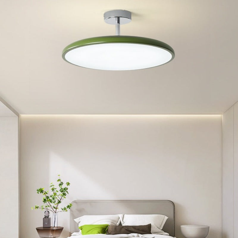 Clérachic green LED disc ceiling light glowing above a bed dressed with a matching olive-green pillow.