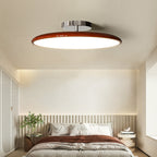Clérachic deep red LED disc ceiling light lit above a bed with warm rust-toned bedding and slatted headboard.