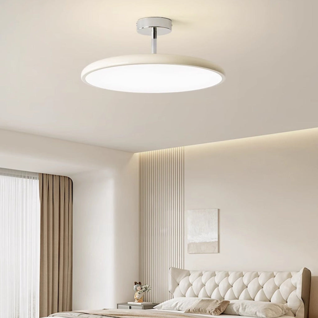 Clérachic cream LED disc ceiling light glowing above a tufted white headboard styled with framed art.