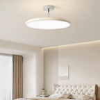 Clérachic cream LED disc ceiling light glowing above a tufted white headboard styled with framed art.