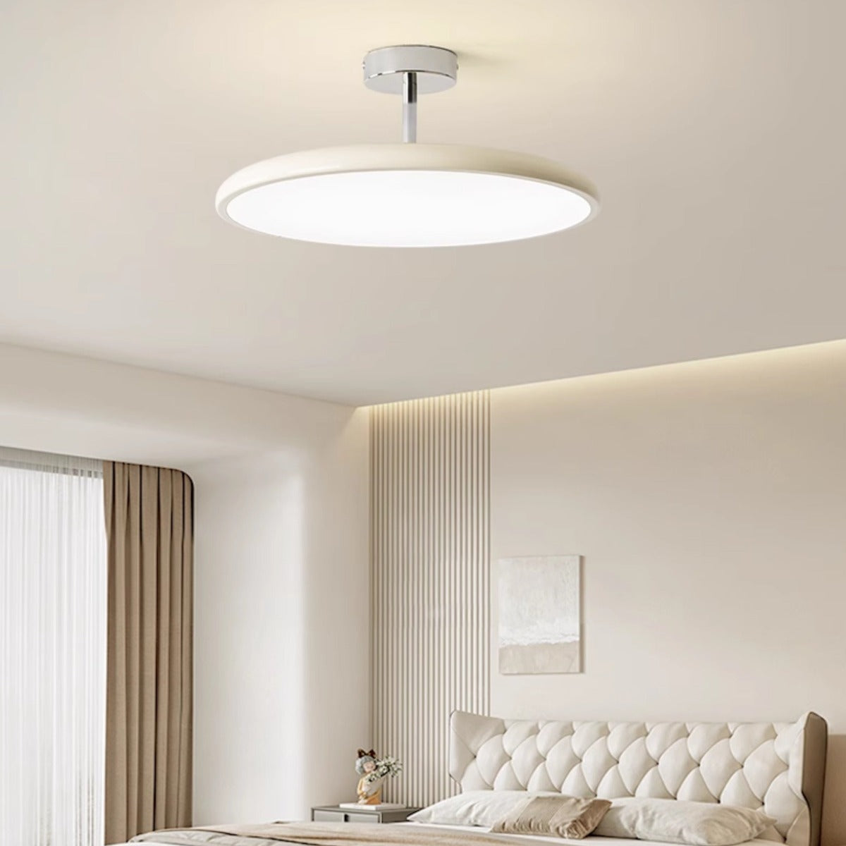 Clérachic cream LED disc ceiling light glowing above a tufted white headboard styled with framed art.