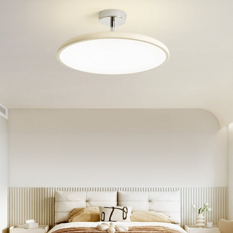 Clérachic cream LED disc ceiling light lit above a minimalist tufted white headboard with a curved wall nook.